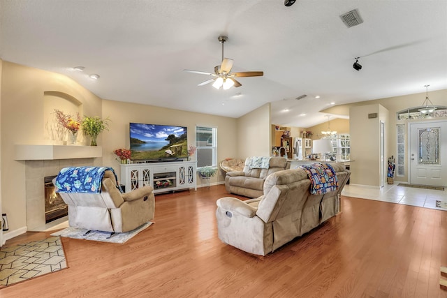 living room with a tiled fireplace, ceiling fan with notable chandelier, vaulted ceiling, and light wood-type flooring