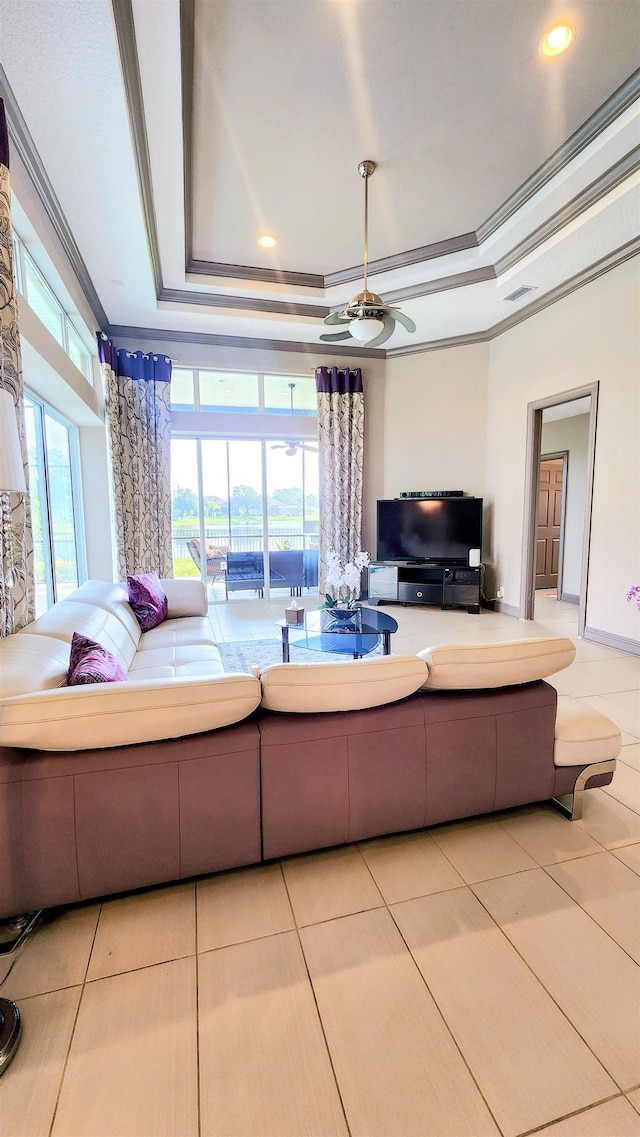 living room featuring a raised ceiling, a wealth of natural light, light tile patterned floors, and ornamental molding