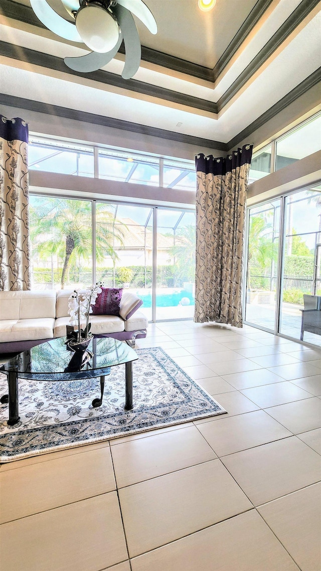 living room with a tray ceiling, crown molding, tile patterned flooring, and a healthy amount of sunlight