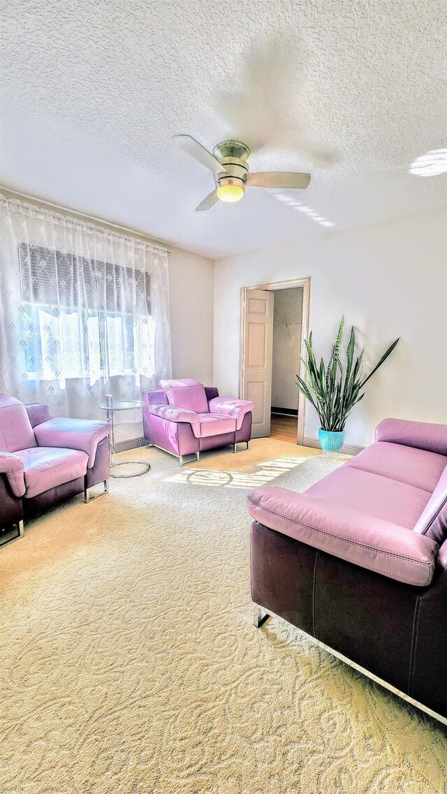 living room featuring ceiling fan, light colored carpet, and a textured ceiling