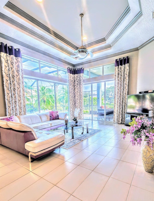 living room featuring ceiling fan, light tile patterned flooring, ornamental molding, and a tray ceiling