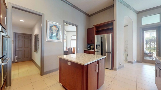 kitchen featuring stainless steel refrigerator with ice dispenser, crown molding, a center island, and light stone counters