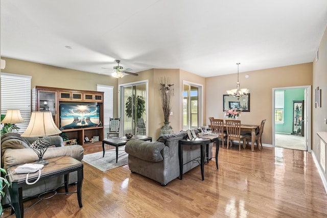 living room featuring ceiling fan with notable chandelier, light wood-type flooring, and a wealth of natural light