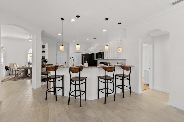 kitchen featuring white cabinets, light stone counters, black appliances, and a breakfast bar