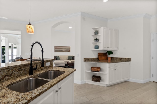 kitchen featuring sink, dark stone counters, white cabinetry, and hanging light fixtures