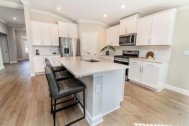 kitchen with vaulted ceiling, stainless steel appliances, a kitchen island with sink, white cabinetry, and sink