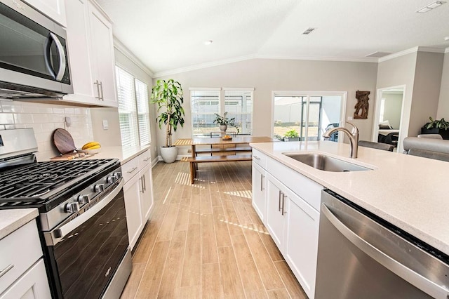 kitchen featuring sink, white cabinets, lofted ceiling, tasteful backsplash, and appliances with stainless steel finishes