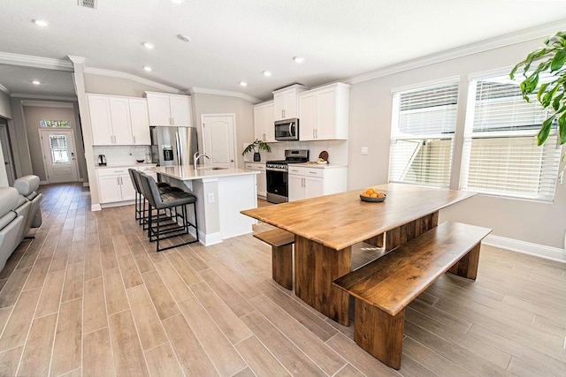 kitchen featuring a kitchen island with sink, appliances with stainless steel finishes, a kitchen bar, decorative backsplash, and white cabinetry