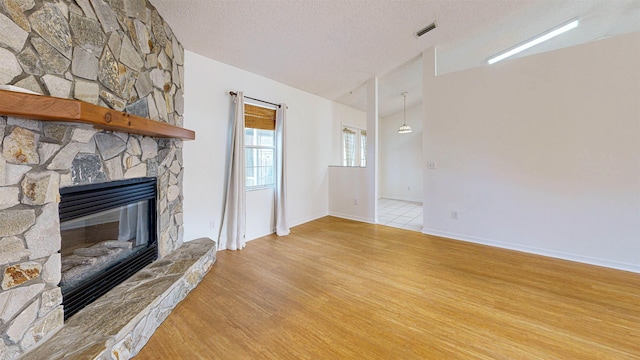 unfurnished living room featuring lofted ceiling, a textured ceiling, a stone fireplace, visible vents, and light wood-type flooring