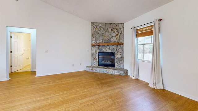 unfurnished living room featuring baseboards, lofted ceiling, a textured ceiling, a stone fireplace, and light wood-type flooring