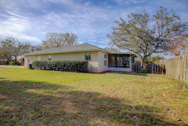 rear view of house featuring a sunroom, a fenced backyard, a lawn, and stucco siding