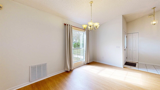 spare room with a chandelier, wood finished floors, visible vents, baseboards, and vaulted ceiling