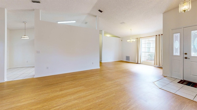 foyer entrance with lofted ceiling, visible vents, light wood-style flooring, an inviting chandelier, and a textured ceiling