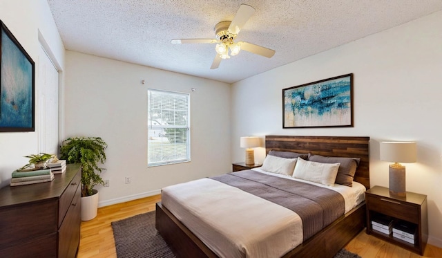 bedroom featuring a textured ceiling, light wood finished floors, a ceiling fan, and baseboards