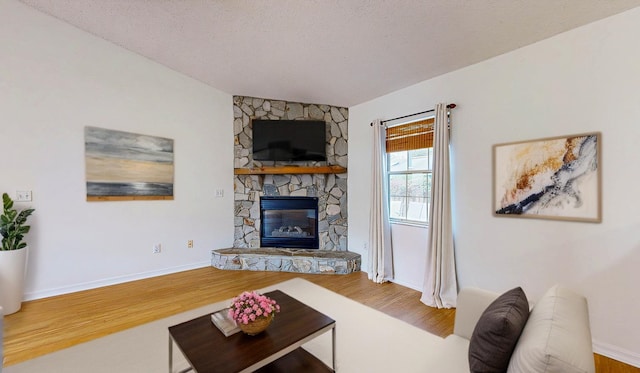 living area featuring a fireplace, a textured ceiling, baseboards, and wood finished floors