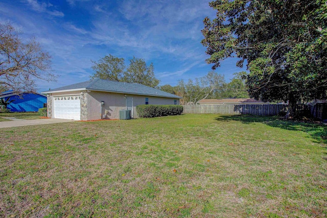 view of yard with a garage, concrete driveway, central AC, and fence