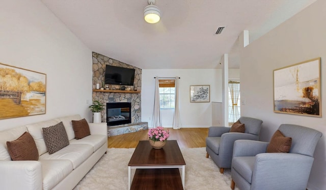 living room featuring lofted ceiling, visible vents, wood finished floors, and a stone fireplace