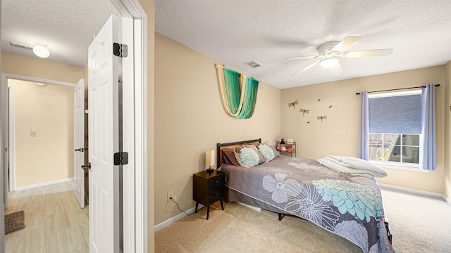 bedroom featuring ceiling fan, light colored carpet, and a textured ceiling