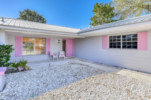 doorway to property with a porch, concrete block siding, and metal roof