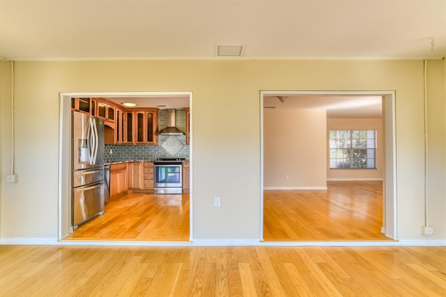 kitchen featuring light wood finished floors, visible vents, wall chimney range hood, decorative backsplash, and appliances with stainless steel finishes