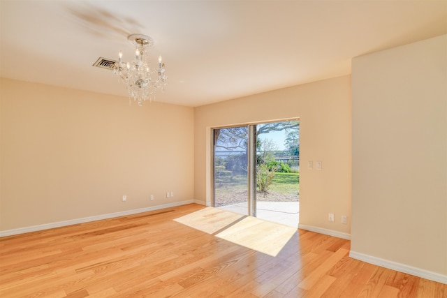 unfurnished room with an inviting chandelier, light wood-style flooring, visible vents, and baseboards