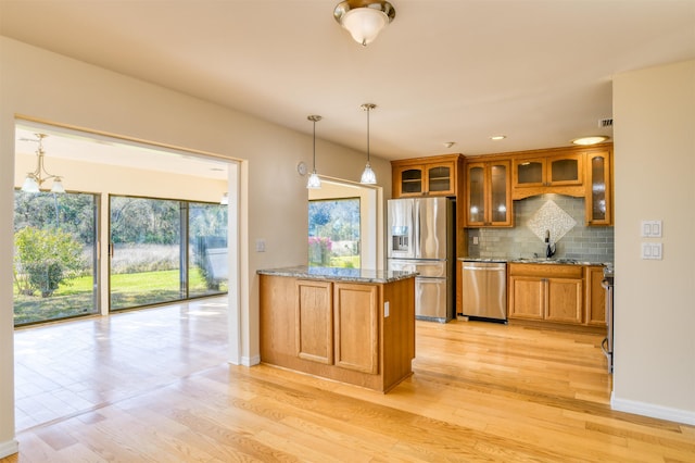 kitchen with light stone counters, decorative backsplash, glass insert cabinets, appliances with stainless steel finishes, and brown cabinets