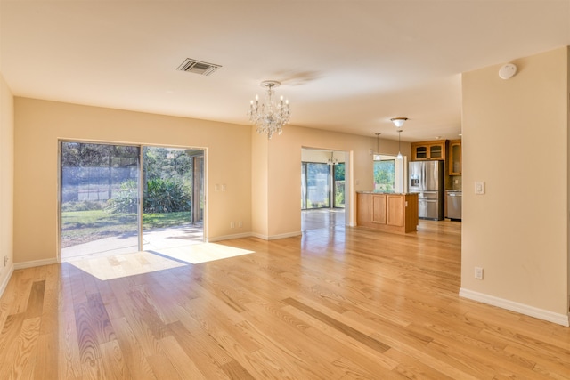 unfurnished room with visible vents, baseboards, a notable chandelier, and light wood finished floors