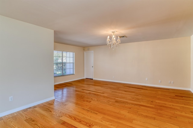 spare room with light wood-style floors, baseboards, a notable chandelier, and visible vents