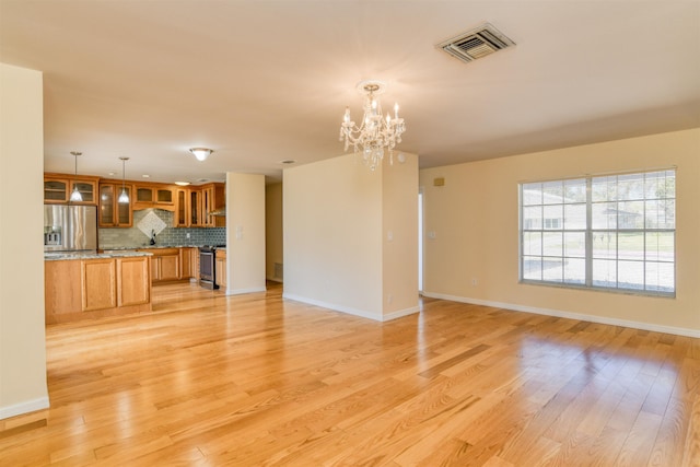 unfurnished living room with visible vents, baseboards, an inviting chandelier, and light wood finished floors