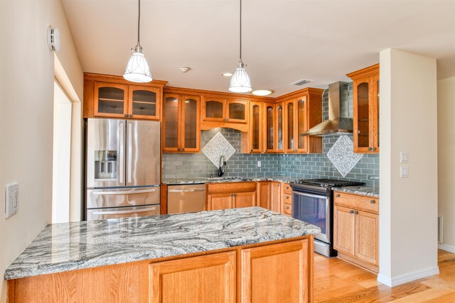 kitchen with light stone countertops, light wood-style flooring, a sink, appliances with stainless steel finishes, and wall chimney range hood