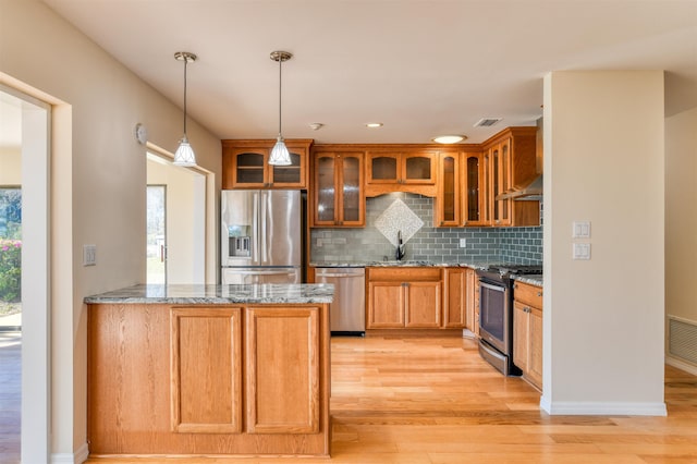 kitchen featuring light stone countertops, light wood finished floors, a sink, appliances with stainless steel finishes, and pendant lighting