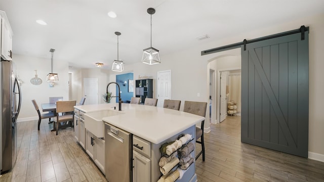 kitchen featuring a breakfast bar, a barn door, light wood-style flooring, stainless steel appliances, and a sink