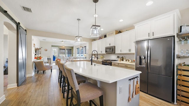 kitchen with visible vents, decorative backsplash, appliances with stainless steel finishes, a kitchen bar, and a barn door