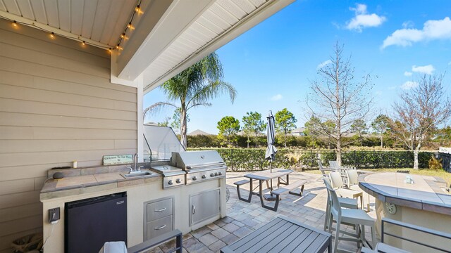 view of patio featuring grilling area, fence, exterior kitchen, and a sink