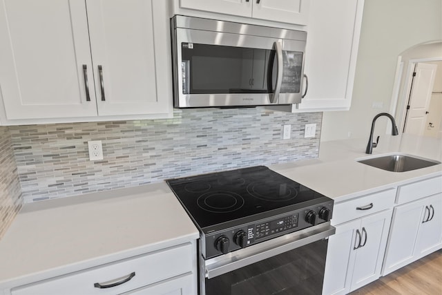 kitchen with a sink, stainless steel microwave, electric range oven, arched walkways, and white cabinets