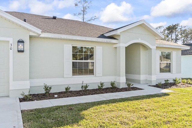 view of front of property featuring stucco siding, a front lawn, and a shingled roof