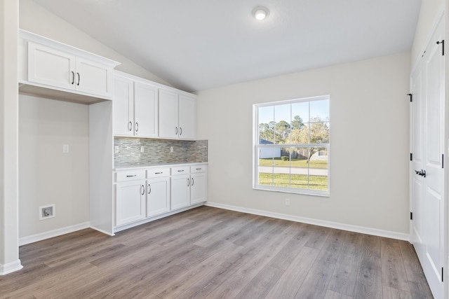 kitchen with backsplash, light countertops, vaulted ceiling, light wood-style flooring, and white cabinetry