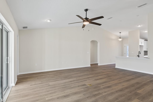 unfurnished living room with visible vents, a ceiling fan, wood finished floors, arched walkways, and lofted ceiling