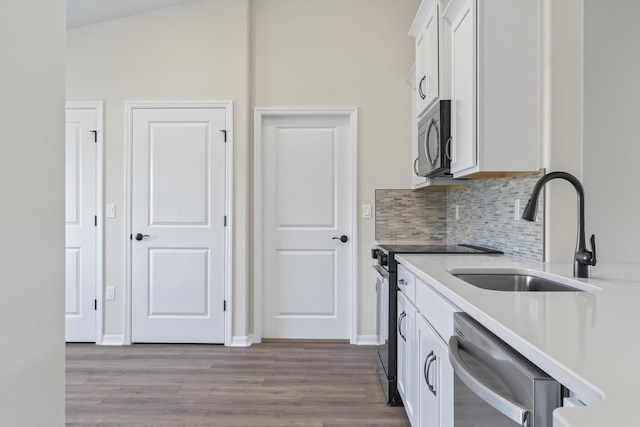 kitchen with wood finished floors, a sink, white cabinets, appliances with stainless steel finishes, and tasteful backsplash