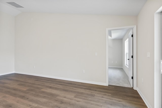 unfurnished room featuring vaulted ceiling, visible vents, baseboards, and wood finished floors