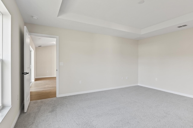 carpeted empty room with visible vents, a raised ceiling, and baseboards