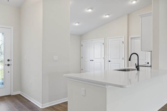 kitchen featuring dark wood-style floors, baseboards, a sink, vaulted ceiling, and light countertops