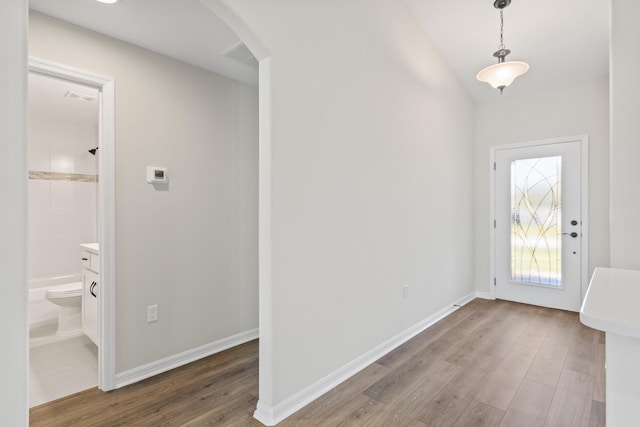 foyer with arched walkways, baseboards, and wood finished floors