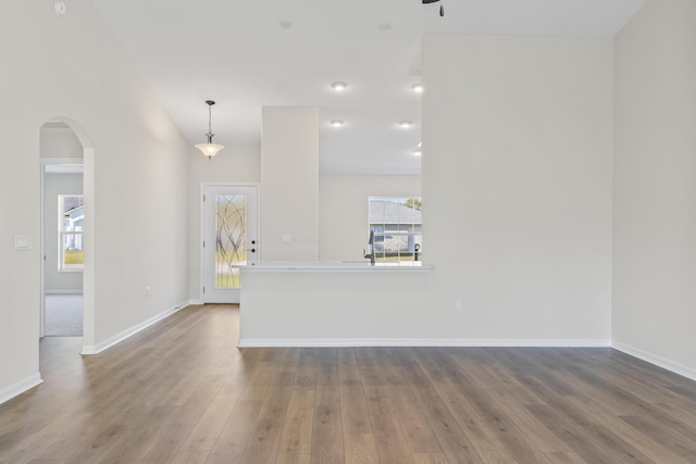 unfurnished living room with a ceiling fan, wood finished floors, arched walkways, and baseboards