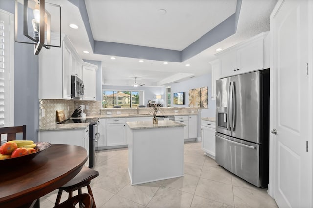 kitchen featuring a raised ceiling, stainless steel appliances, a kitchen island, and white cabinetry