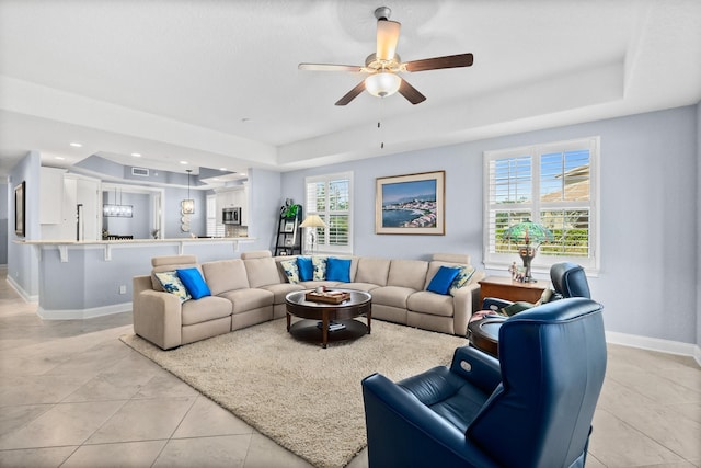 living area featuring light tile patterned floors, a raised ceiling, a wealth of natural light, and baseboards