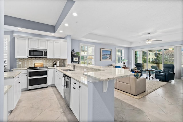 kitchen with a peninsula, white cabinets, open floor plan, appliances with stainless steel finishes, and a tray ceiling