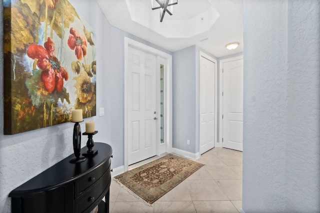 foyer featuring a raised ceiling, a textured wall, baseboards, and light tile patterned floors