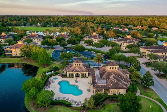 aerial view at dusk with a water view and a view of trees