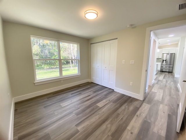 unfurnished bedroom featuring light wood-type flooring, stainless steel refrigerator with ice dispenser, and a closet